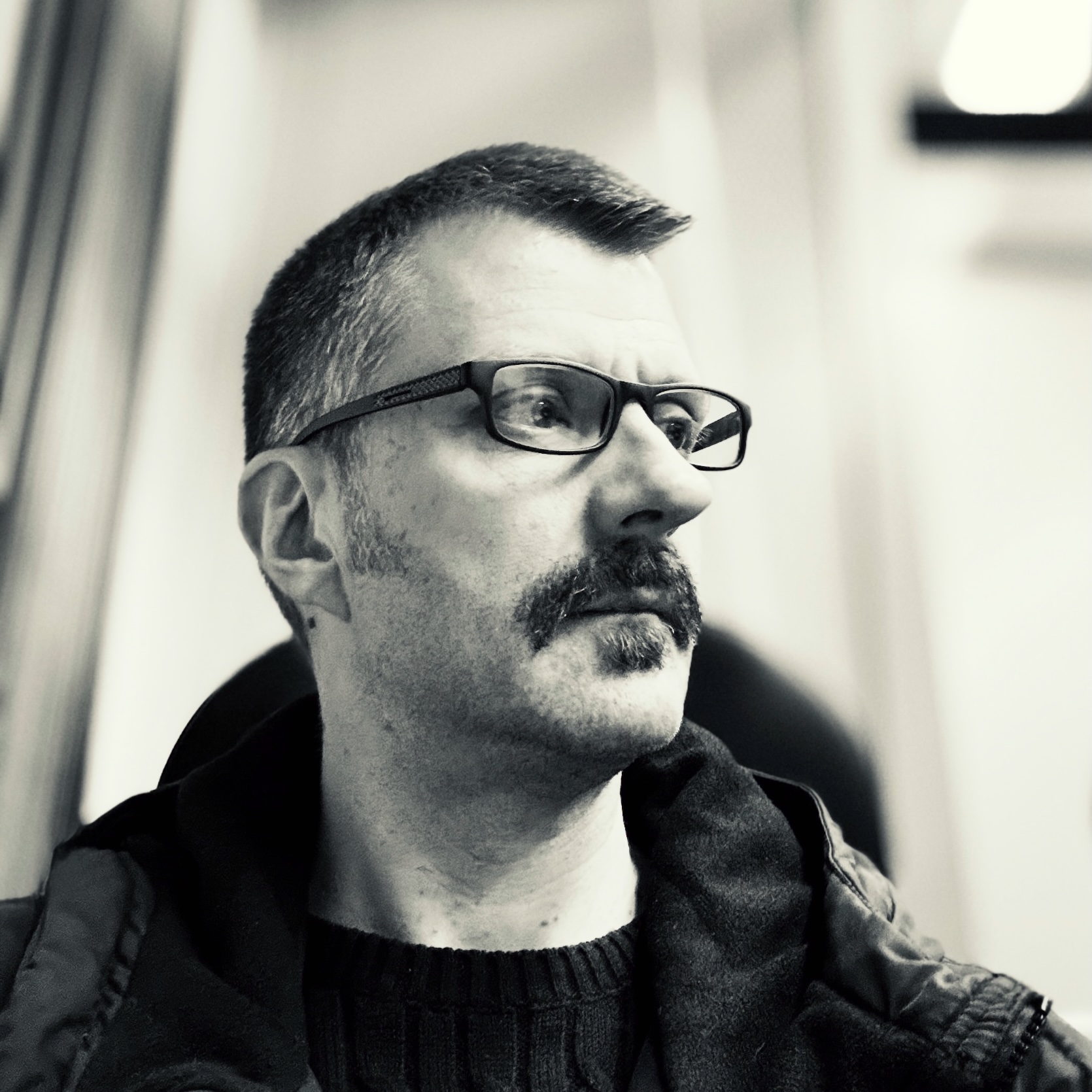 A black and white photograph of John Topley wearing sunglasses sat in front of a brick wall